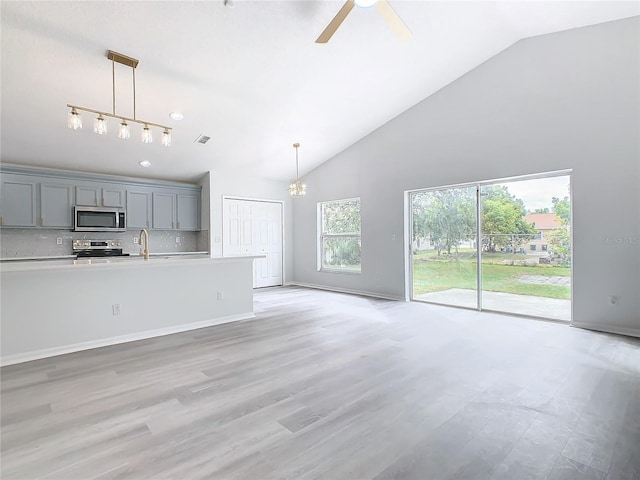 unfurnished living room with ceiling fan with notable chandelier, sink, high vaulted ceiling, and light wood-type flooring