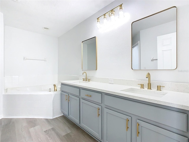 bathroom with tiled bath, hardwood / wood-style flooring, and vanity