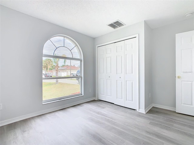 unfurnished bedroom with light hardwood / wood-style floors, a textured ceiling, and a closet