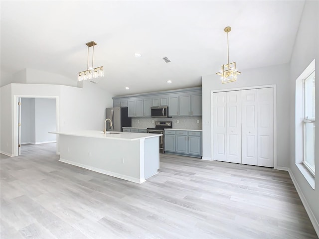 kitchen with tasteful backsplash, a center island with sink, hanging light fixtures, gray cabinetry, and stainless steel appliances