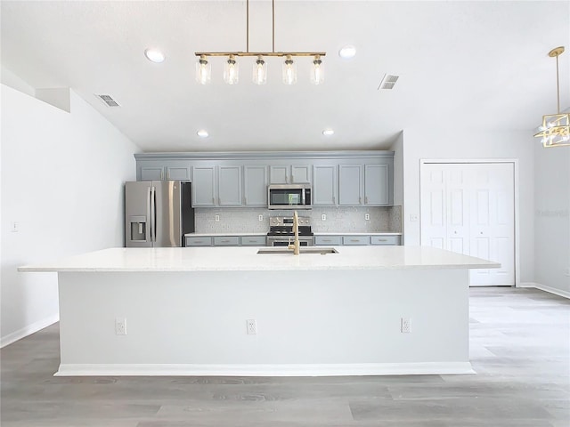 kitchen with appliances with stainless steel finishes, pendant lighting, and an island with sink