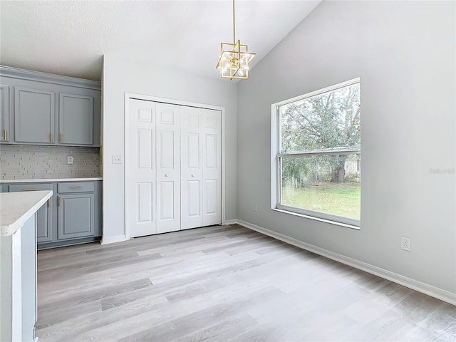 kitchen featuring tasteful backsplash, lofted ceiling, gray cabinets, light hardwood / wood-style flooring, and a chandelier