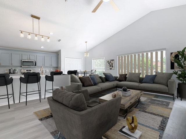 living room with high vaulted ceiling, ceiling fan with notable chandelier, light hardwood / wood-style flooring, and sink