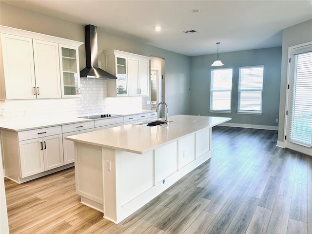 kitchen with sink, a center island with sink, white cabinets, and wall chimney range hood