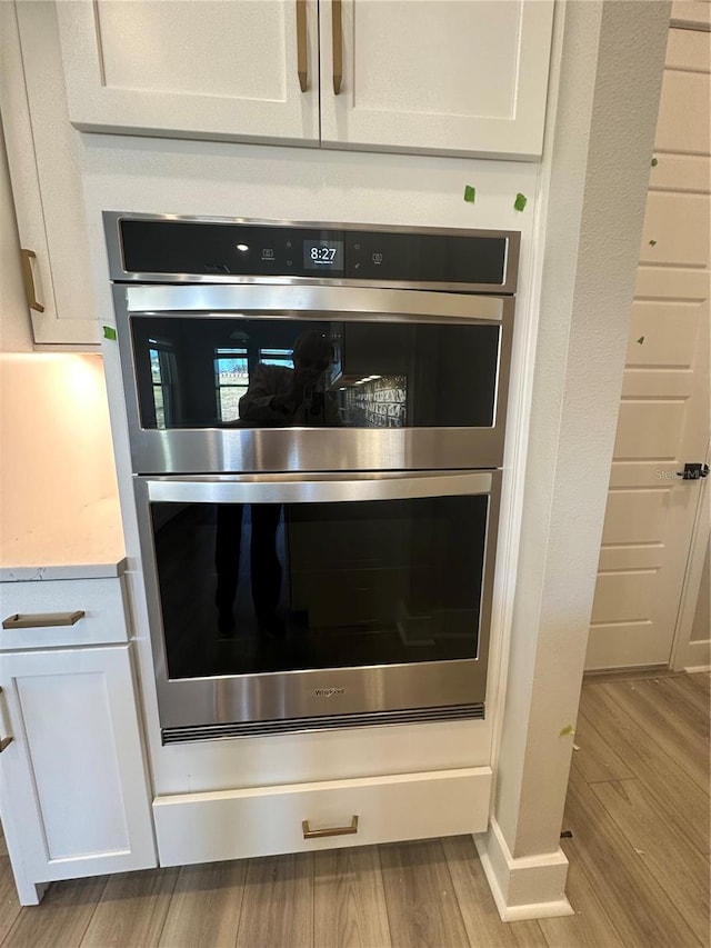 interior details with double oven, white cabinetry, light wood-type flooring, and light stone counters