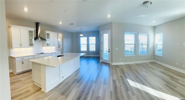 kitchen featuring sink, wall chimney range hood, light wood-type flooring, and white cabinetry