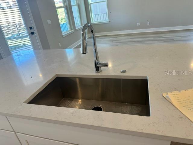 room details featuring sink, white cabinetry, and light stone counters