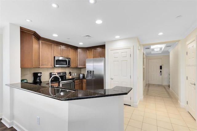 kitchen with kitchen peninsula, decorative backsplash, dark stone countertops, and stainless steel appliances