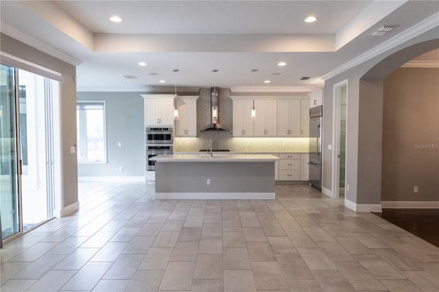 kitchen featuring wall chimney exhaust hood, a center island with sink, white cabinets, and stainless steel appliances