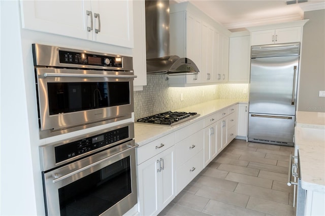 kitchen featuring light stone counters, white cabinetry, wall chimney range hood, and stainless steel appliances