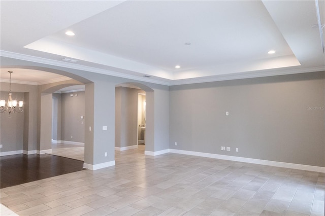 empty room featuring a tray ceiling, ornamental molding, and a chandelier