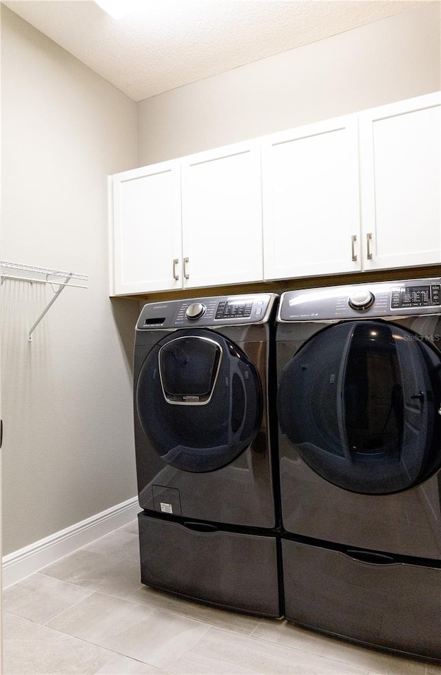 clothes washing area with washing machine and clothes dryer and cabinets