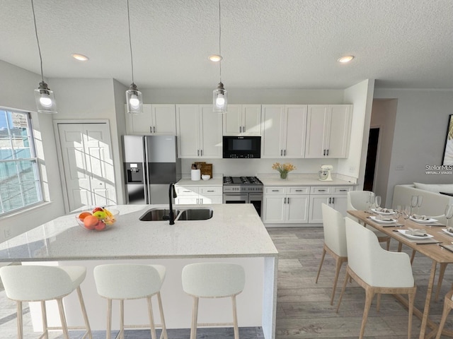 kitchen featuring stainless steel appliances, white cabinetry, a center island with sink, and sink