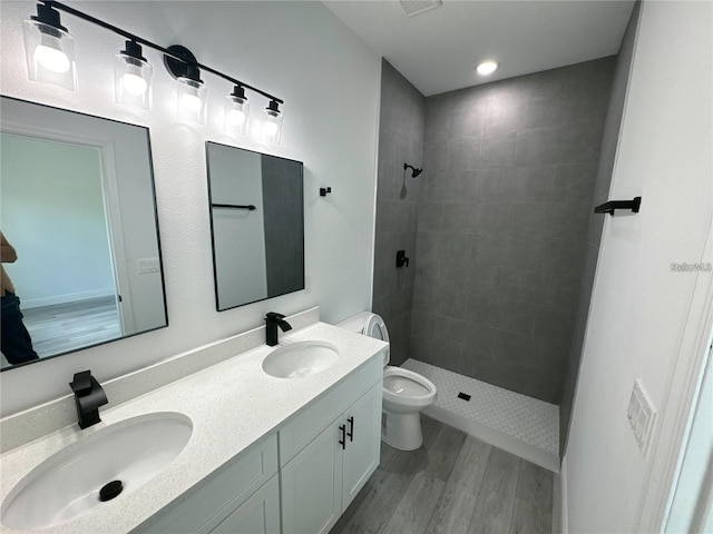 bathroom with tiled shower, hardwood / wood-style floors, vanity, and toilet