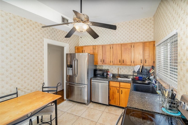 kitchen with sink, light tile patterned flooring, ceiling fan, dark stone counters, and appliances with stainless steel finishes