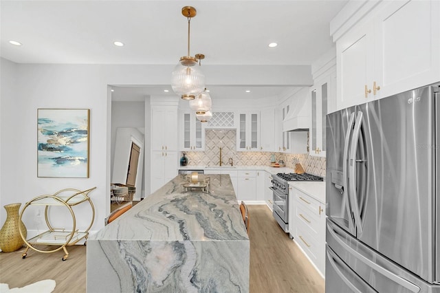 kitchen with stainless steel appliances, light stone countertops, decorative backsplash, white cabinetry, and decorative light fixtures