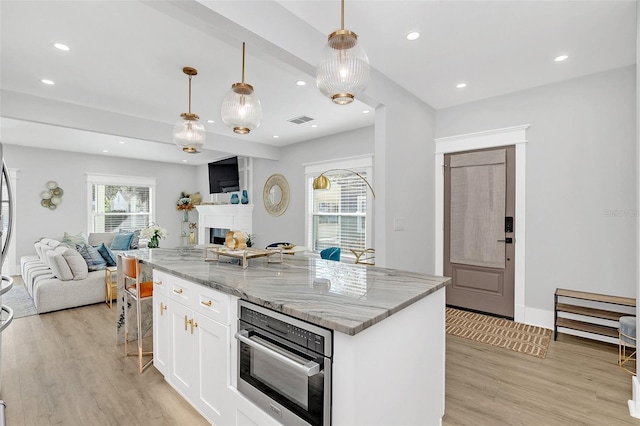 kitchen featuring light stone countertops, stainless steel oven, a center island, decorative light fixtures, and white cabinetry