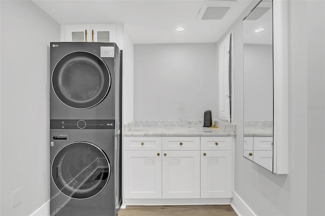 laundry area featuring stacked washer and dryer, cabinets, and wood-type flooring