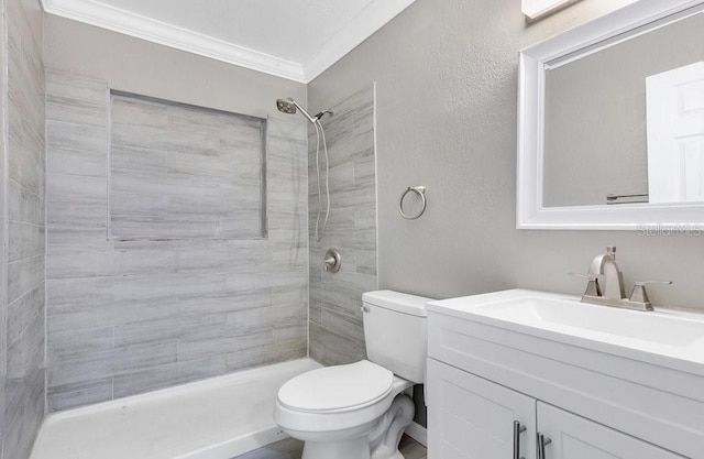 bathroom featuring a tile shower, vanity, toilet, and crown molding