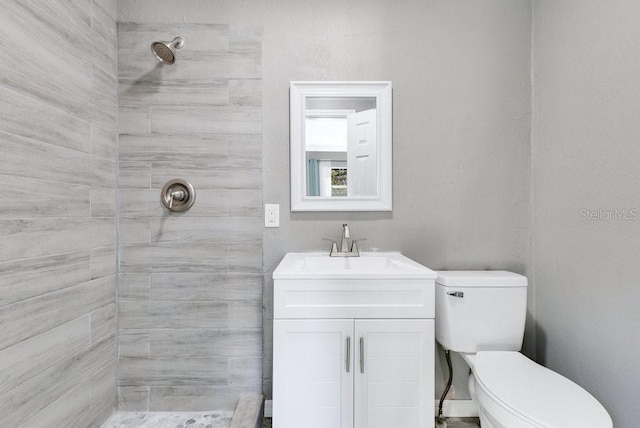 bathroom featuring a tile shower, vanity, and toilet