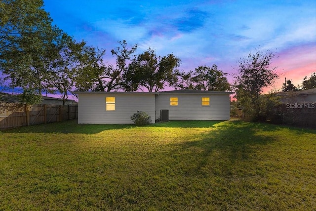 back house at dusk featuring central AC unit and a yard