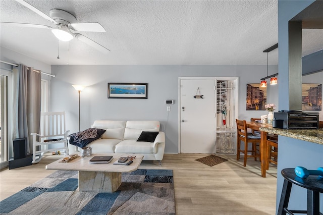 living room with ceiling fan, light hardwood / wood-style flooring, and a textured ceiling