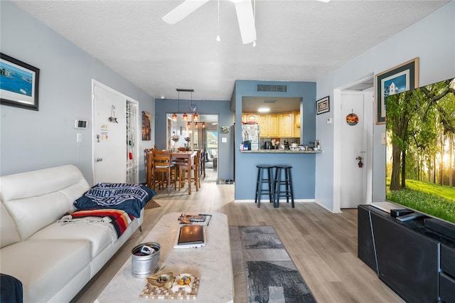 living room with ceiling fan, light hardwood / wood-style flooring, and a textured ceiling