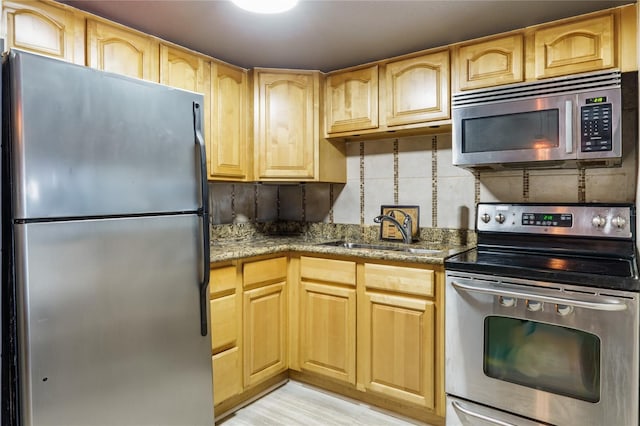 kitchen with sink, dark stone counters, light hardwood / wood-style floors, decorative backsplash, and appliances with stainless steel finishes