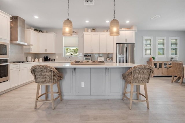 kitchen featuring stainless steel appliances, a center island, decorative light fixtures, and wall chimney exhaust hood