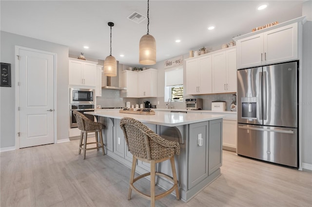 kitchen with pendant lighting, light hardwood / wood-style flooring, appliances with stainless steel finishes, white cabinetry, and a center island