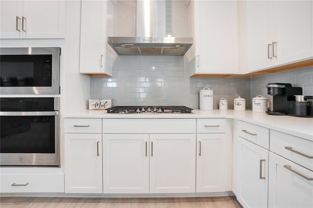 kitchen with tasteful backsplash, wall chimney range hood, stainless steel appliances, and white cabinets