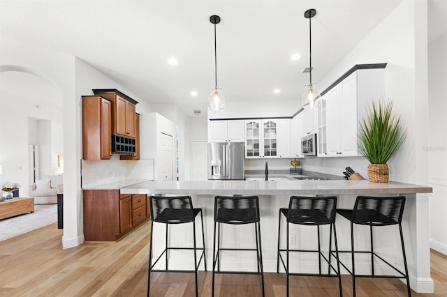 kitchen with hanging light fixtures, appliances with stainless steel finishes, a breakfast bar, white cabinets, and light wood-type flooring