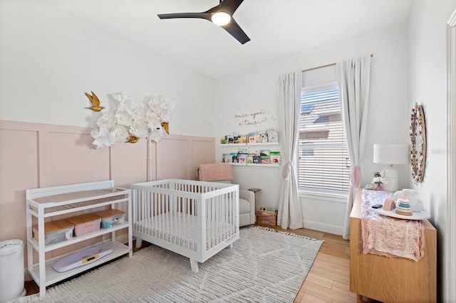 bedroom with hardwood / wood-style floors, ceiling fan, and a crib