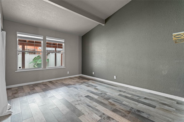 spare room featuring a textured ceiling, light hardwood / wood-style flooring, and vaulted ceiling with beams