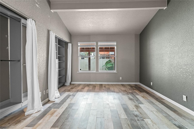 unfurnished room with vaulted ceiling with beams, a textured ceiling, and light hardwood / wood-style floors