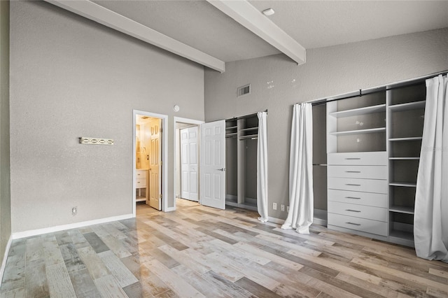 unfurnished bedroom featuring beamed ceiling, a high ceiling, connected bathroom, and light hardwood / wood-style flooring