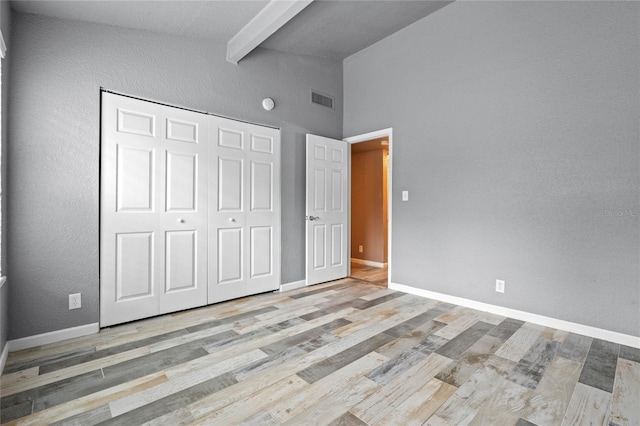 unfurnished bedroom featuring high vaulted ceiling, a closet, beam ceiling, and light wood-type flooring