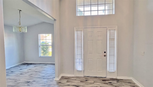 foyer entrance with lofted ceiling, light hardwood / wood-style flooring, and an inviting chandelier