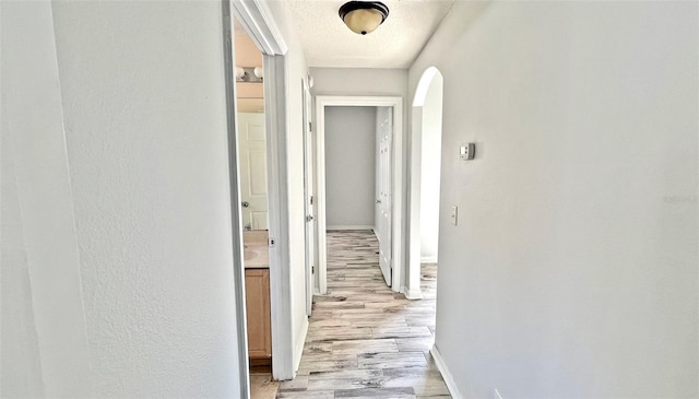 hallway with a textured ceiling and light hardwood / wood-style flooring