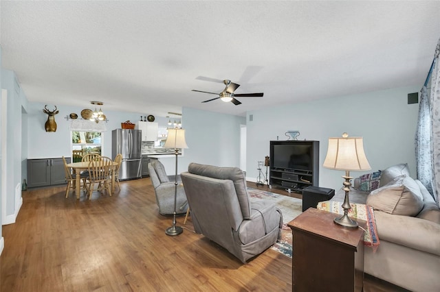 living room with wood-type flooring, ceiling fan with notable chandelier, and a textured ceiling