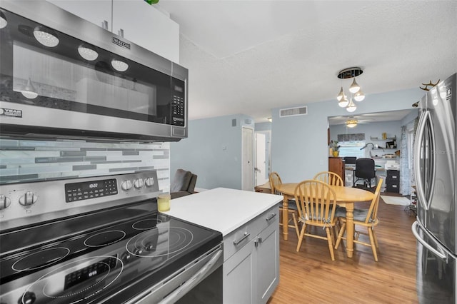 kitchen featuring appliances with stainless steel finishes, decorative light fixtures, decorative backsplash, a textured ceiling, and light hardwood / wood-style flooring