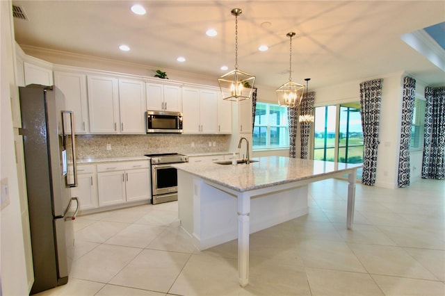 kitchen featuring decorative light fixtures, appliances with stainless steel finishes, white cabinetry, a sink, and an island with sink