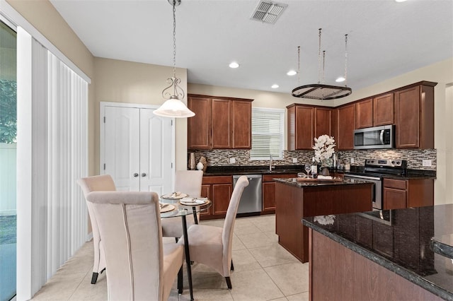 kitchen featuring a kitchen island, appliances with stainless steel finishes, pendant lighting, tasteful backsplash, and dark stone counters