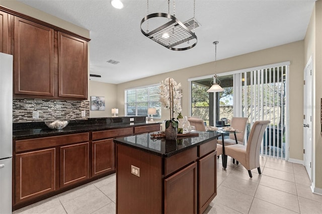 kitchen with decorative light fixtures, a center island, light tile patterned floors, dark stone countertops, and decorative backsplash