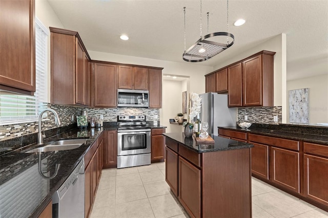 kitchen with sink, dark stone countertops, stainless steel appliances, a center island, and light tile patterned flooring