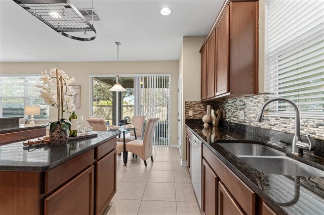 kitchen with sink, light tile patterned floors, a wealth of natural light, dark stone counters, and backsplash