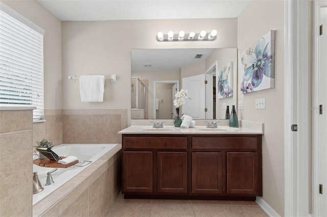 bathroom with a relaxing tiled tub, vanity, and tile patterned floors