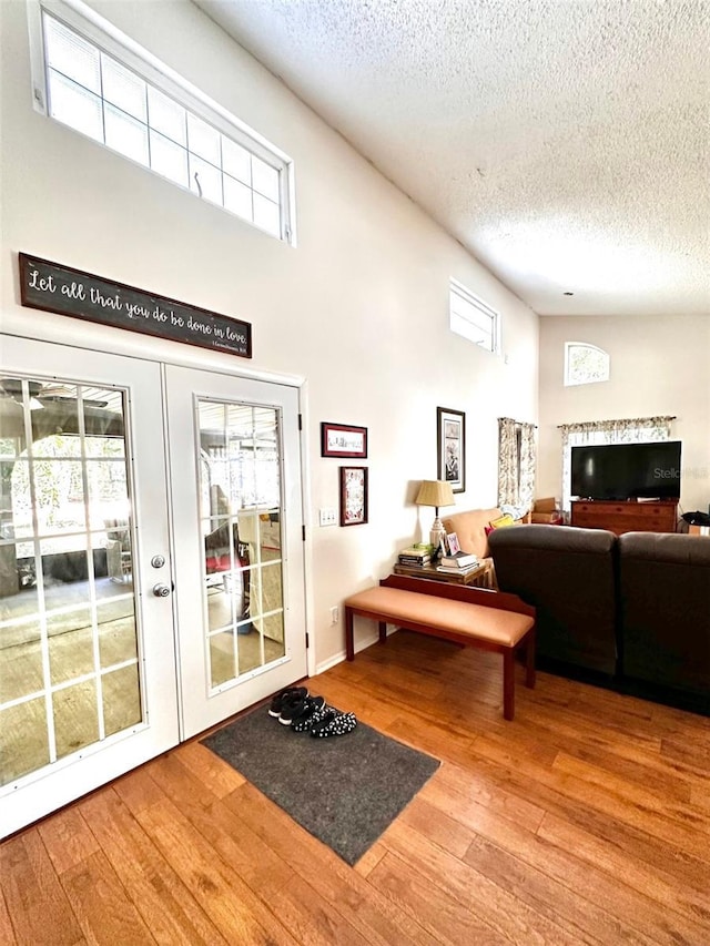 interior space with hardwood / wood-style floors, a towering ceiling, a textured ceiling, and french doors