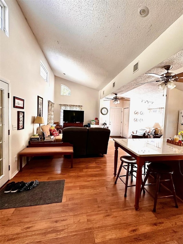 dining area with wood-type flooring, a textured ceiling, plenty of natural light, and lofted ceiling