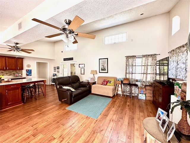 living room featuring a healthy amount of sunlight, light wood-type flooring, a textured ceiling, and a high ceiling